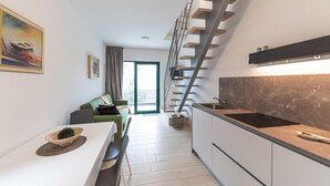 A modern kitchen with a built-in stove, a dining area with a table and chairs, and a staircase leading to a balcony. - 2 bedroom beach front home in Okrug Gornji (Okrug Gornji)