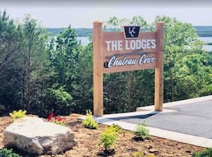 A wooden sign for "The Lodges Chateau Cove" with a view of trees and a body of water in the background. - Table Rock Lake View! Two Community Pools! (Branson)