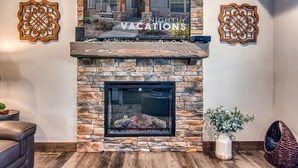 A stone fireplace with a TV above it, a decorative wall piece, and a wicker chair. - Table Rock Lake View! Two Community Pools! (Branson)