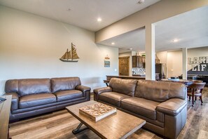 Un salon avec deux canapés en cuir marron, une table basse en bois et, au fond, un coin cuisine.