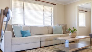 A modern living room with a beige sectional sofa, a glass coffee table, and a striped rug. - Vineyard Cottage - Your Innkeeper Mudgee (Eurunderee)