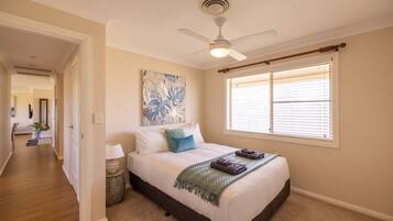 A bedroom with a bed, a ceiling fan, a window with blinds, and a painting on the wall.