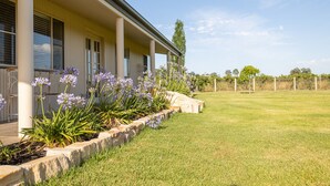A building with a covered porch, a well-maintained lawn, and flowering plants. - Vineyard Cottage - Your Innkeeper Mudgee (Eurunderee)
