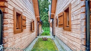 Un étroit couloir en bois, avec un petit espace verdoyant au centre, bordé de deux bâtiments dotés de portes et de fenêtres en bois.