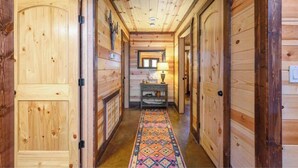 A wooden hallway with a patterned carpet, a small table with a lamp, and a mirror on the wall. - Over Yonder-3Bed/Bunks/Pool Table/3.5 Bath (Broken Bow)