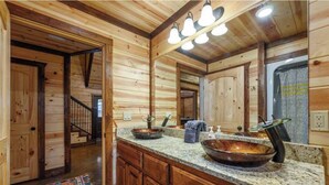 A wooden cabin interior with a large mirror, a granite countertop, and a rustic bathroom. - Over Yonder-3Bed/Bunks/Pool Table/3.5 Bath (Broken Bow)
