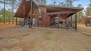 A rustic cabin with a large porch, a staircase leading to the upper level, and a covered outdoor seating area. - Over Yonder-3Bed/Bunks/Pool Table/3.5 Bath (Broken Bow)