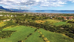 Un pueblo costero con zonas residenciales y agrícolas, una extensa masa de agua y montañas a lo lejos.