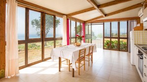 Un coin repas avec une table dressée pour deux personnes, de grandes fenêtres et une vue sur le paysage.