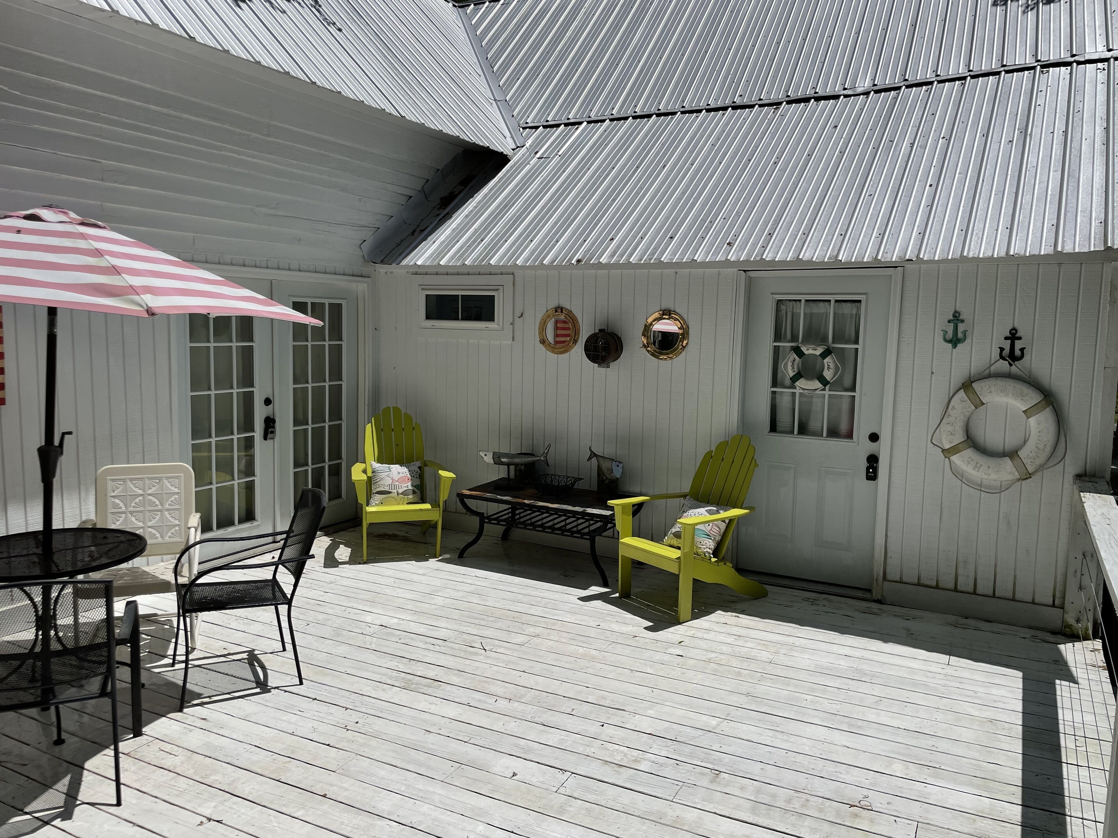 Terraza exterior cubierta con mesa y sillas, una puerta y un flotador en la pared.