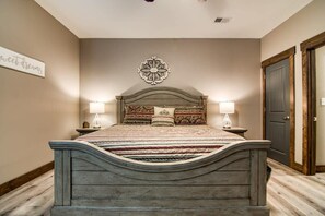 A bedroom with a wooden bed, two bedside lamps, a decorative wall piece, and a door. - Gorgeous Table Rock Lake View! Hot Tub, Pool! (Branson)