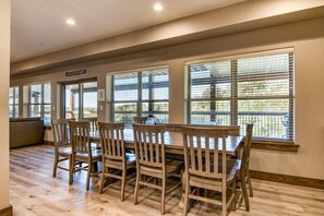 A dining area with a wooden table and chairs, large windows with blinds, and a sign above the door. - Gorgeous Table Rock Lake View! Hot Tub, Pool! (Branson)