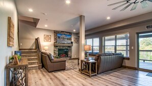 A spacious living area with a fireplace, a staircase, and a large window providing a view of the outdoors. - Gorgeous Table Rock Lake View! Hot Tub, Pool! (Branson)