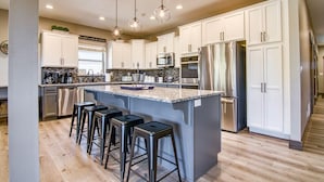 A modern kitchen with white cabinets, stainless steel appliances, and a central island with bar stools. - Gorgeous Table Rock Lake View! Hot Tub, Pool! (Branson)