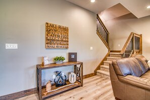 A living room with a wooden console table, a leather sofa, a staircase, and a wall with a motivational quote. - Gorgeous Table Rock Lake View! Hot Tub, Pool! (Branson)