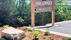 A wooden sign for "The Lodges Chateau Cove" with a view of trees and a body of water in the background. - Gorgeous Table Rock Lake View! Hot Tub, Pool! (Branson)