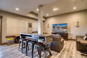 A modern living room with a bar area, a large TV, and a comfortable seating arrangement. - Gorgeous Table Rock Lake View! Hot Tub, Pool! (Branson)