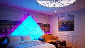 Habitación de hotel con cama, mesita de noche, un cuadro en la pared y una lámpara de techo original.