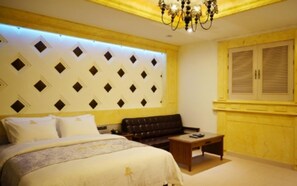 A bedroom with a bed, a sofa, a small table, a decorative wall panel, and a window with shutters. - Dongtan Windsor Hotel (Hwaseong)