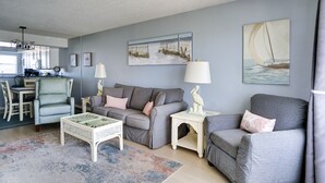Una sala de estar con un sofá gris, una mesa de centro blanca y un comedor con una silla y una mesa.