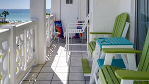 Un balcón con barandillas blancas, sillas verdes y blancas, una mesa y vista al océano.