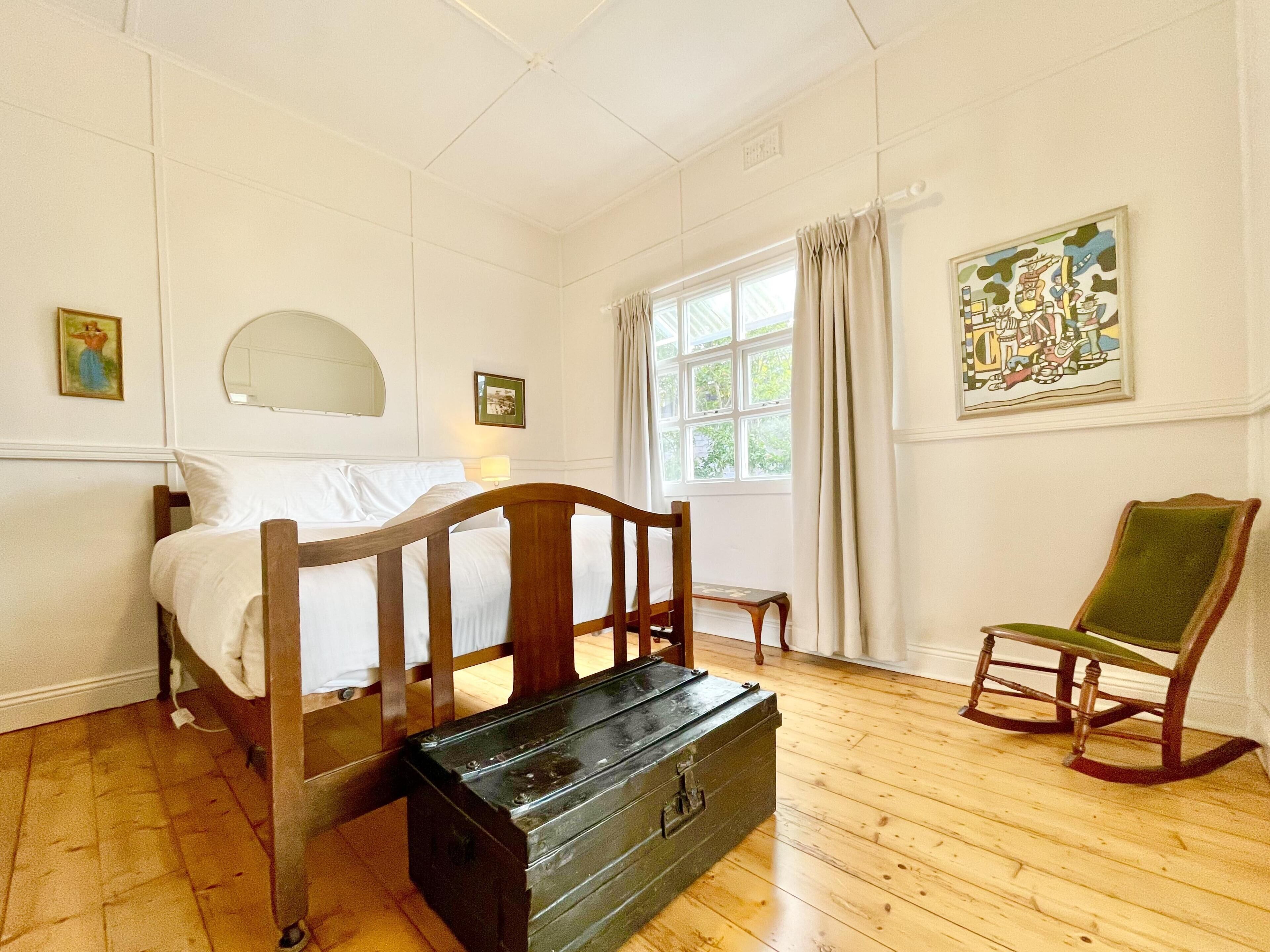 A bedroom with a wooden bed, a green armchair, a small table, and a window with curtains.