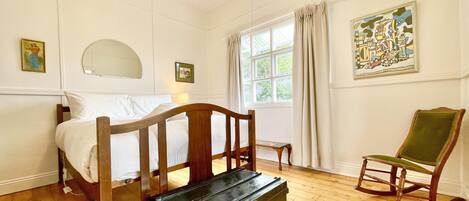 A bedroom with a wooden bed, a green armchair, a small table, and a window with curtains.