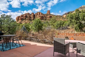 An outdoor patio with wicker furniture, a stone wall, and a view of red rock formations.
