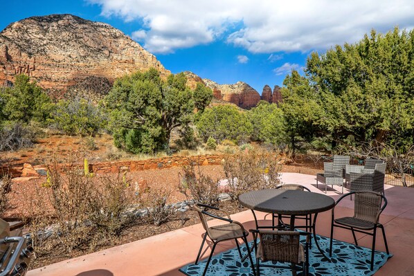 An outdoor patio with a table and chairs, surrounded by desert vegetation and a mountain backdrop.