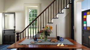 A dining area with a wooden table, a vase of flowers, and a fruit bowl. - Brisbane House: Restored Historic Stone House in the Country (Arena)
