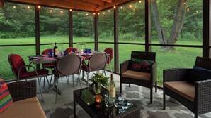 An enclosed patio area with a table set for dining, wicker furniture, and a view of a grassy landscape. - Brisbane House: Restored Historic Stone House in the Country (Arena)