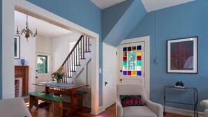 A living room with a staircase, a green table, a white armchair, and a colorful stained glass door. - Brisbane House: Restored Historic Stone House in the Country (Arena)