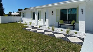 A modern white house with a number 697, a patio with a bench and cushions, and a garden with a white fence and greenery. - Casa del Mare - Beautiful Naples Pool Home (Naples)