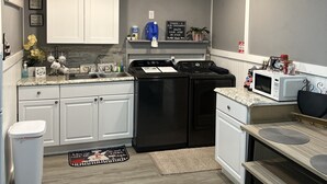 A compact kitchen with white cabinets, a black dishwasher, a microwave, and a sink. There are decorative items on the counter and a small rug on the floor. - Guesthouse studio Generac backup powered w washer&dryer. Fully equipped. (Spring)