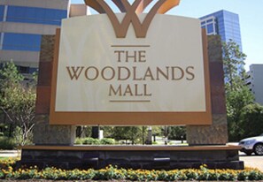 A sign for The Woodlands Mall with a modern design and a stone base.