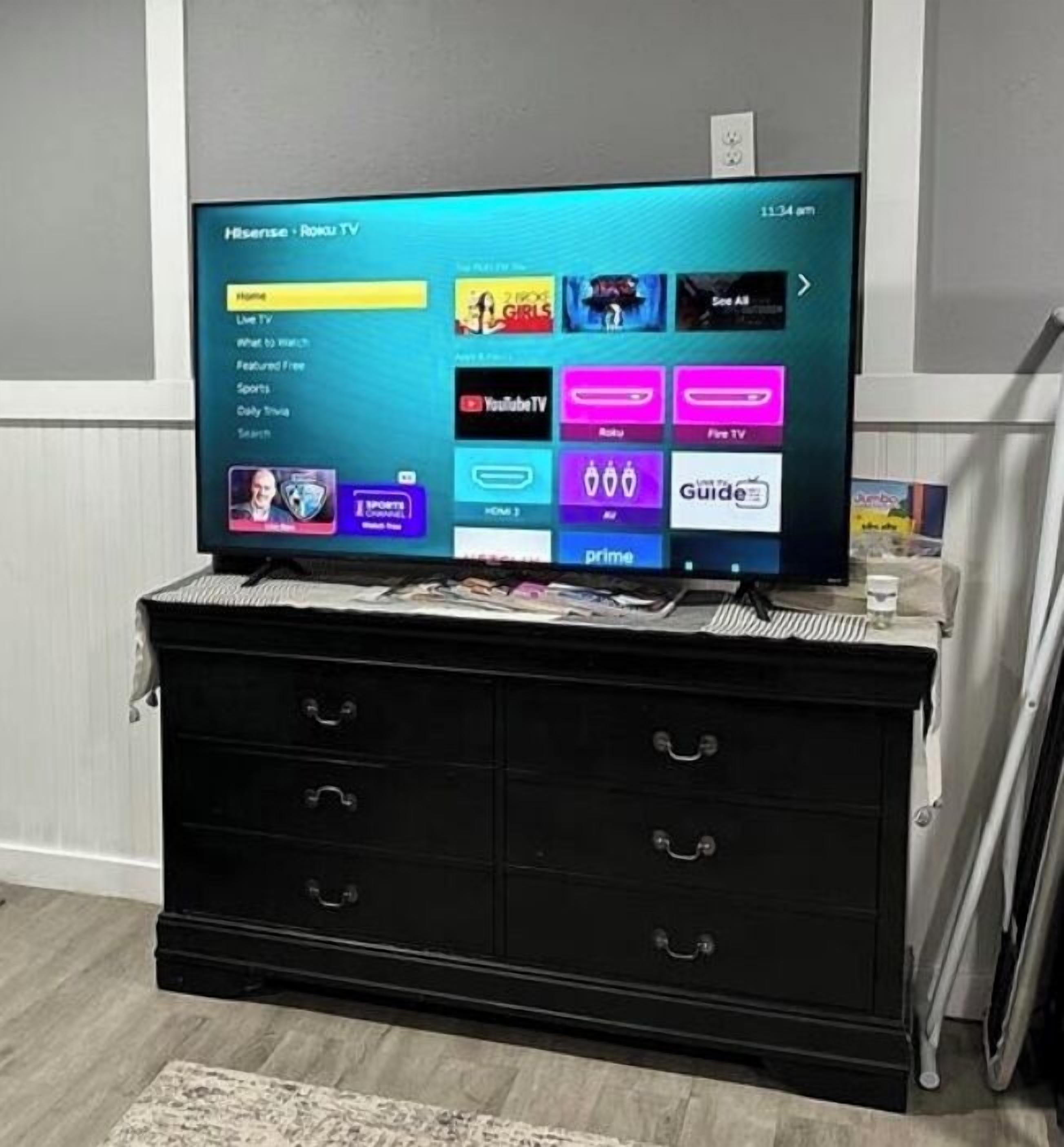Un téléviseur à écran plat posé sur une commode noire, et l’interface du menu des chaînes télé est visible.