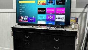 Un téléviseur à écran plat posé sur une commode noire, et l’interface du menu des chaînes télé est visible.