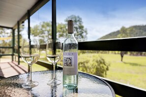A bottle of wine and two glasses on a table with a view of a green landscape.