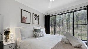 Un lit bien fait, avec du linge de lit blanc, une table de chevet avec une lampe et deux tableaux encadrés accrochés au mur.