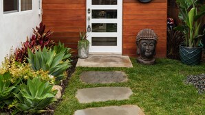 Une maison moderne avec une façade en bois, une porte blanche et un petit jardin agrémenté d’un chemin de pierres menant à la porte.