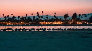 Une plage au crépuscule, avec des palmiers et des bâtiments en arrière-plan.