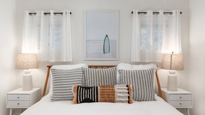 Une chambre à coucher bien rangée, avec un lit, deux tables de chevet et un tableau accroché au mur.
