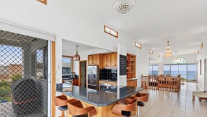 Une cuisine moderne dotée d’un îlot central, de tabourets de bar en bois et offrant une vue sur la mer.