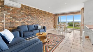 Un salon moderne avec un mur en briques, un ensemble de canapés bleus, une table basse et une vue sur l’extérieur.
