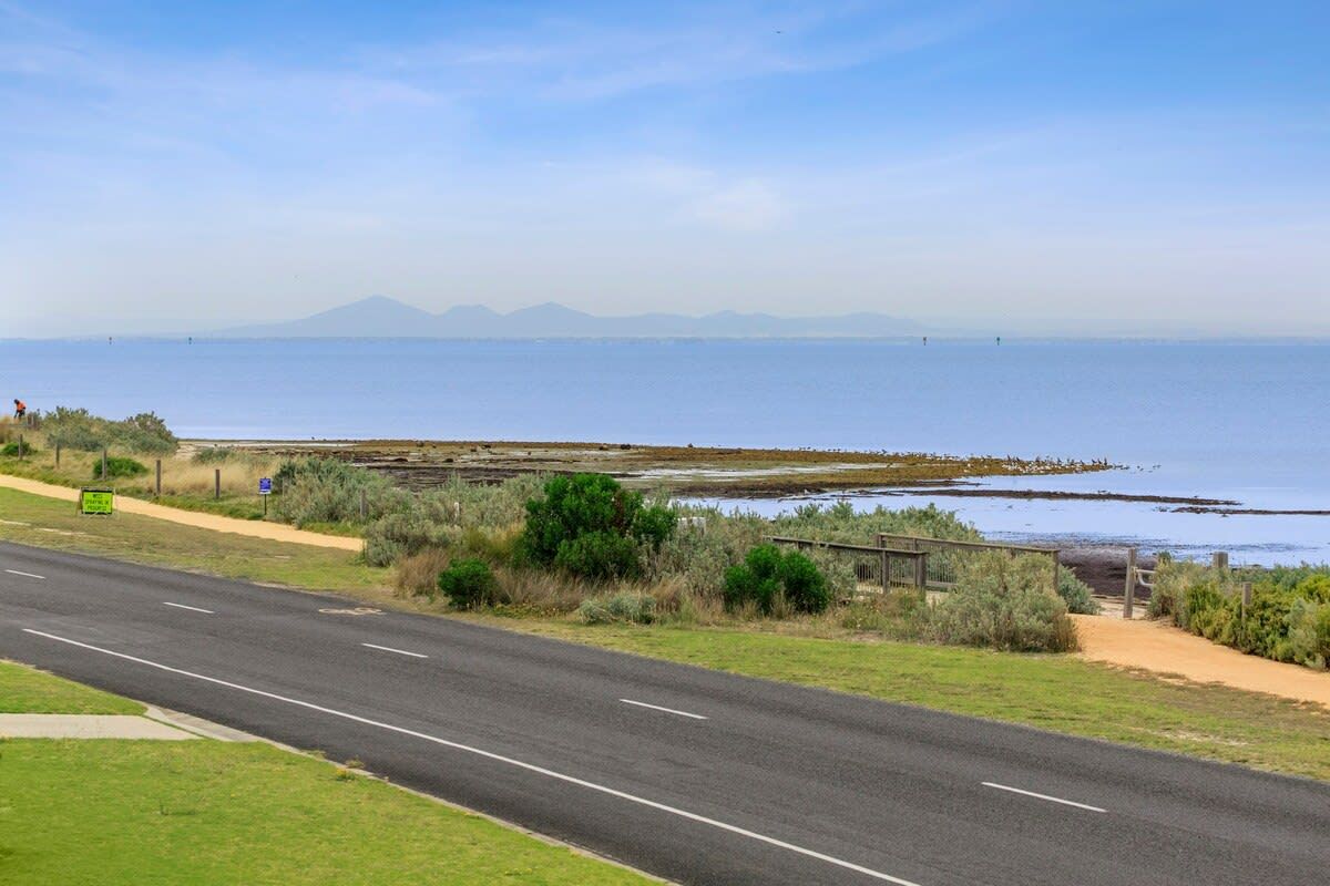 A coastal road with a clear view of the ocean and distant mountains.