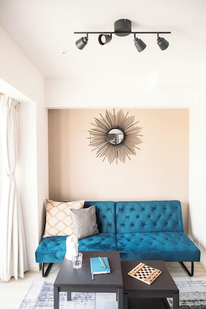 A modern living room with a blue sofa, a coffee table, a chessboard, and a wall-mounted mirror.