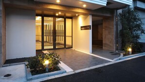 A modern hotel entrance with a gated door, a sign indicating the name, and a small garden area with plants. -  Section L Residence Asakusa East  (Tokyo)