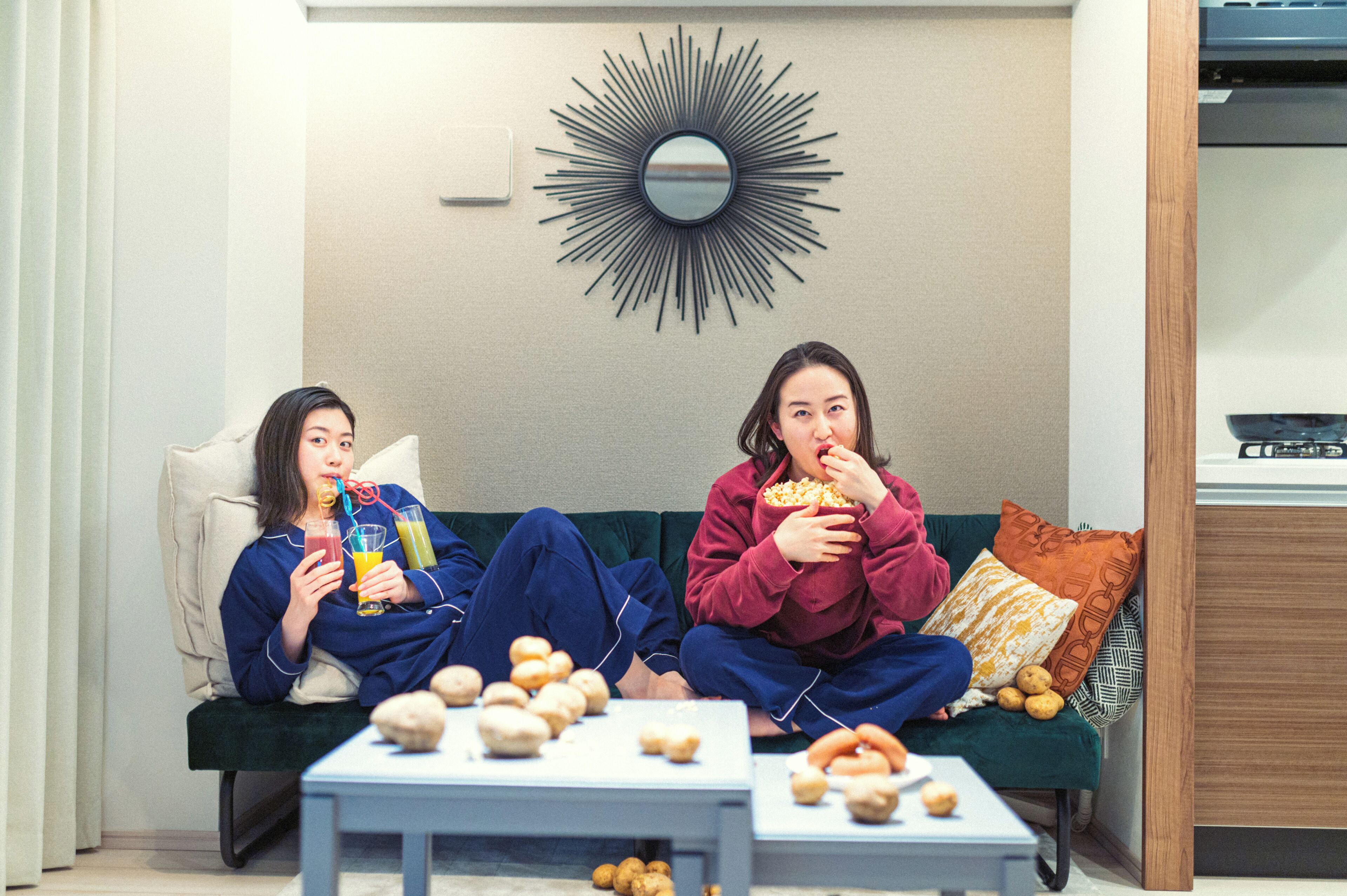Two individuals seated on a sofa with a coffee table in front of them, a wall-mounted mirror, and a television on a stand.