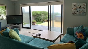 Sala de estar com televisão, sofá e porta de vidro deslizante que dá para um jardim.