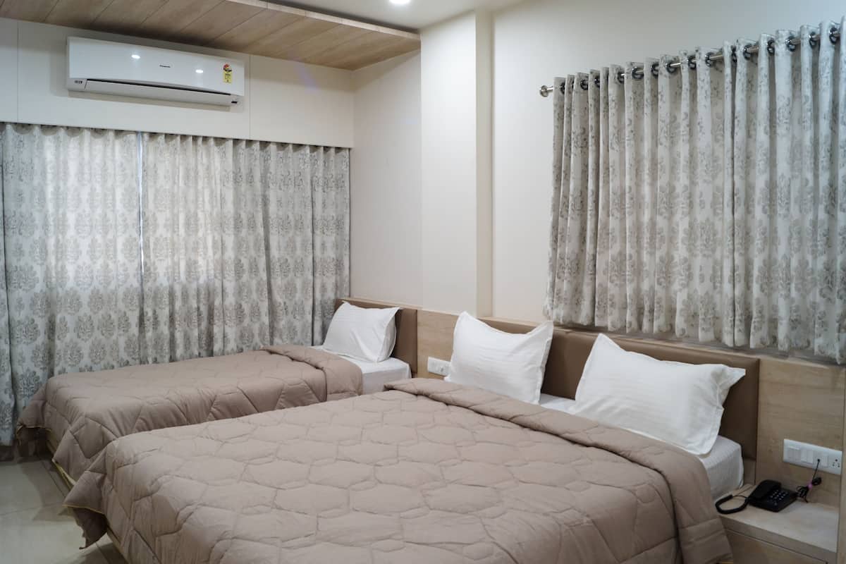 Habitación de hotel con dos camas, ropa de cama color beige, un equipo de aire acondicionado y cortinas estampadas.